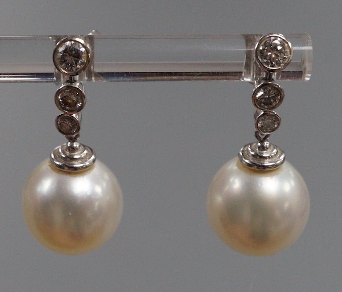 A modern pair of 750 white metal, singe stone South Sea pearl and graduated three stone diamond set drop earrings, overall 22mm, gross weight 6.8 grams